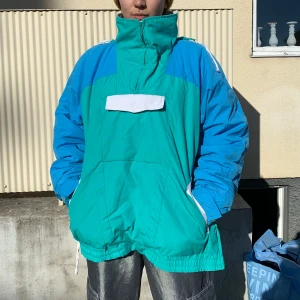 Anorak med dold huva - En jättefin och varm anorak. Ficka på magen och två fickor med dragkedjor i sidorna. En dragkjedja på ena sidan för enklare på och avtagning. Gott skick.