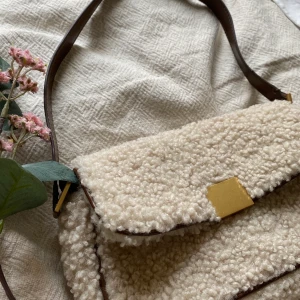 Lurvig axelremsväska - Axelremsväska i teddymaterial med detaljer i läderimitation. Väskan har ett stort fack och även ett mindre för exempelvis kort. Helt nyskick pga. Aldrig använd. Budning i kommentarerna (avslutas 4/3, 21:00)🧚🏻‍♀️