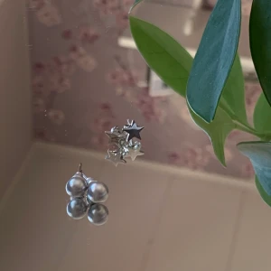 Två silvriga örhängen - Två par silvriga örhängen (inte riktigt silver), ett par med stjärnor och ett annat med en ”gråaktig boll”. Säljer då jag inte använder dem. Lite använda, men i ganska bra skick. Frakt ingår EJ i priset. 