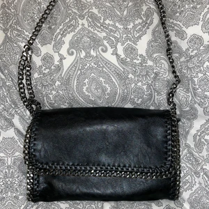Handväska i skinn - Svart handväska i skinn med axelrem i silver. Stängs med dragkedja och med magnetisk knapp. I begagnat men fint skick! . Säljer för 60kr