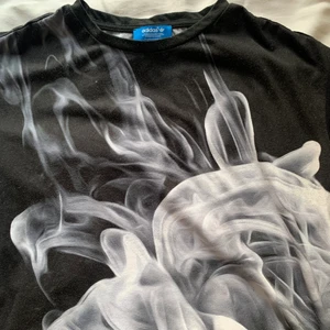 Adidas T-shirt  - Adidas T-shirt från Rita Ora kollektion. Den är svart med rök mönster både fram och baksida, med även adidas logga på baksida. Mesh på armarna. 