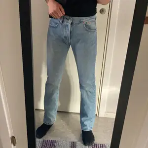 Ett par ljusblå Levis’s jeans i modellen 501. Storlek 30/30. Det saknas ett bälteshål framtill men det går fortfarande lika bra att ha ett bälte ändå. 