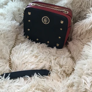 Tommy Hilfiger väska  - Säljer nu min fina Tommy Hilfiger väska då den ej kommer till användning. Guld detaljer med guld kedja. Innerficka finns i bakre facket. Väskan hänger på höften på mig som är 172 cm lång 💕 H 15 cm L 16.5 cm D 6.5  Kan mötas i Stockholm samt frakta, köparen står då för frakten.