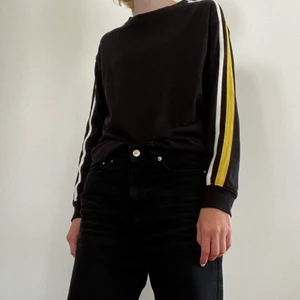 Svart sweatshirt med revärer - En svart sweatshirt med gula och vita revärer längst ärmarna, från H&Ms dividedavdelning. Använd ett fåtal gånger. Tveka inte att kontakta mig vid frågor!