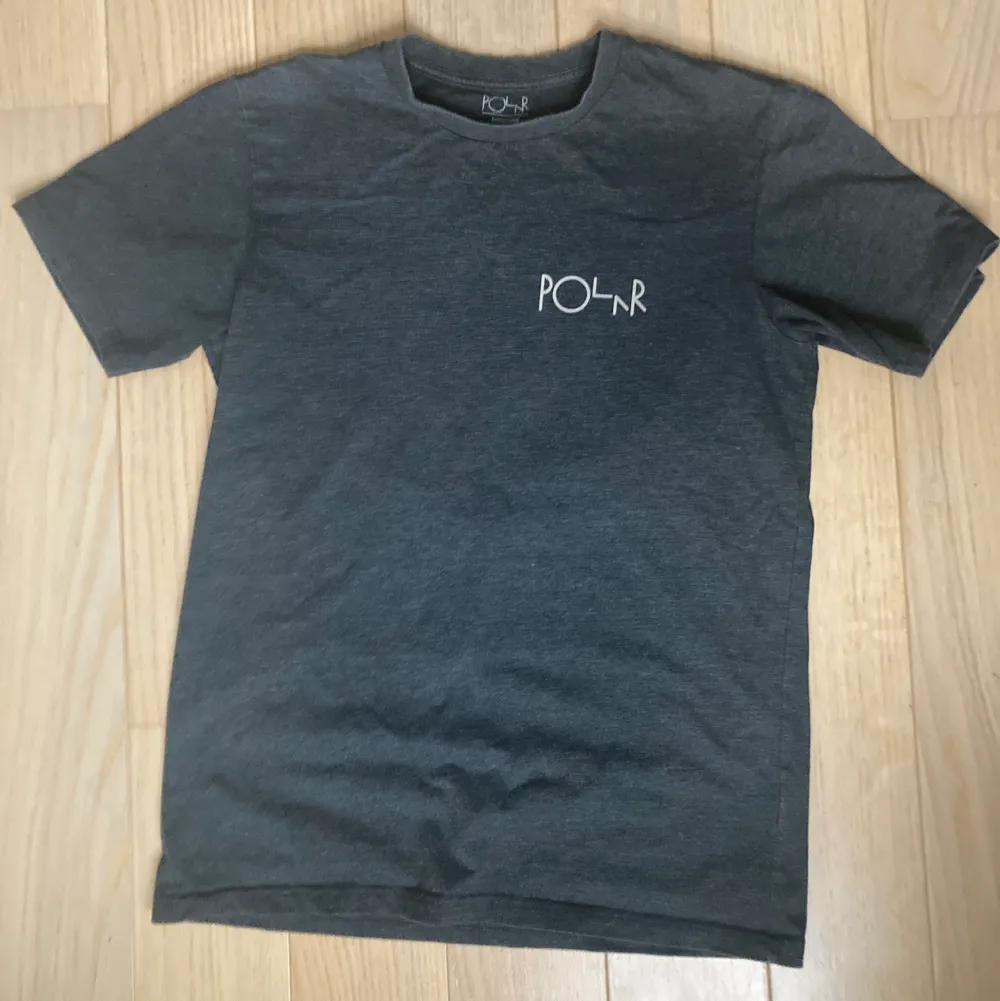 Mörkgrå T-shirt från skatemärket Polar med turkost tryck på ryggen. Köpare står för frakt och modellen är 180 för referens.. T-shirts.