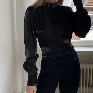 Svart topp - Svart glansig topp från Nakd med öppen rygg som man knyter nertill i strl 36. Aldrig använd med lappen kvar. Frakt tillkommer! 