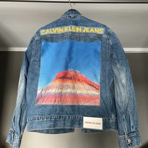 Calvin Klein Jeansjacka - Säljer denna riktigt unika jeansjacka från Calvin Klein med mountain print på ryggen! Sålde slut fort. Storlek medium och är true to size. Skicket är riktigt bra även fast jackan är använd. Nypris runt 1800kr. Hör av er vid möjliga pris förslag eller annat!