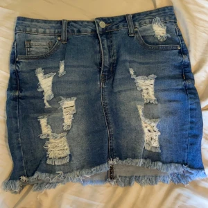 Midwaist jeanskjol med slitningar - Sitter som en smäck, stretchig skönt jeanstyg. Kjolen har en del slitningar framtill och några baktill. 