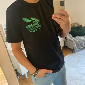 Svart t-shirt med grönt tryck, ord pris 500kr 
