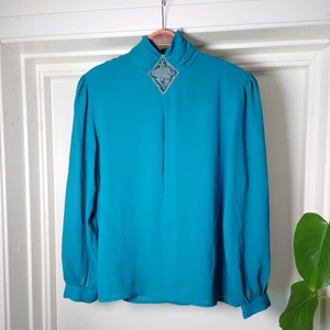 Vintageblus - Turkos vintageblus med fina detaljer. Spets vid halsen. Små små axelvaddar som är väldigt lätta att ta bort om man vill det. Ingen storleksmärkning men bör vara M🍒