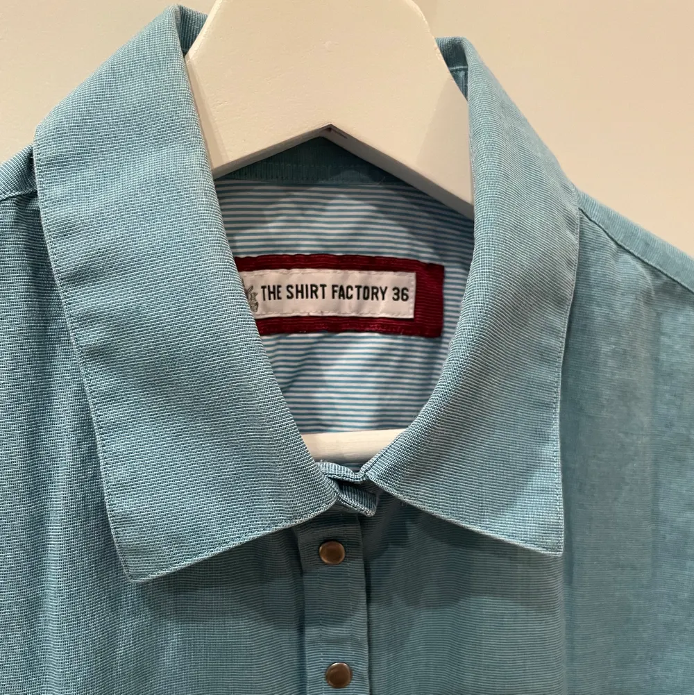 Blå skjorta i fint skick från The Shirt Factory i storlek 36 med tryckknappar.. Skjortor.