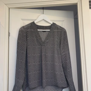Svart/vit/grå blus från Gina Tricot - Svart, vit, grå blus, topp, från Gina Tricot.  V-ringad. Storlek 36. ❣️ Knappdetaljer vid händerna och man kan välja att vika upp där knapparna sitter eller låta ärmen ”hänga”. 👍🏼 Mycket bra skick! Inga defekter. 🥰 Frakt tillkommer (51 kr) 🤍