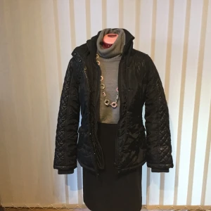 Jacka style Ricci - Skön och tuff javka med snygga detaljer med skärp. Stickad ribbad halskrage. En paspoalknäppning med dragkedja och tryckknappar. Ficklock är försedd med ttvå tryckknappar., ribbad och stickad handledsmudd.  Längd 68 cm, är,längd 63 cm. Från vänster axel till höger axel 37 cm. Tar swish