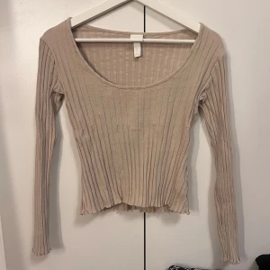 Beige ribbad långärmad topp - En beige ribbad långärmad topp med rund halsringning. Modellen är tight och har en lätt croppad passform med vågig kant nertill. Passar Xs-S.