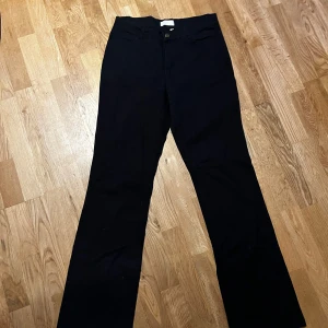 Svarta Jeans - Snygga svarta byxor med en klassisk design. De har en rak passform och är perfekta för en stilren look. Byxorna har fickor både fram och bak samt en knapp och dragkedja i midjan.