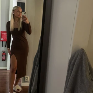 Brun långärmad klänning med slits - Säljer en snygg brun långärmad klänning med figurnära passform och hög slits på ena sidan. Perfekt för dig som vill ha en stilren och trendig look. Klänningen har rund halsringning och är i ett mjukt material.