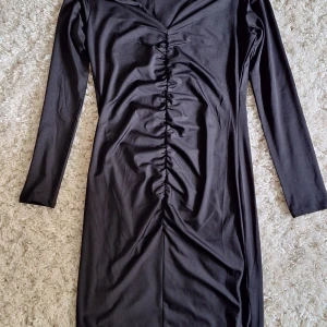 Svart långärmad klänning med rynk från H&M - Svart klänning från H&M med långa ärmar och snygg rynkdetalj. V-ringad hals och figurnära modell.