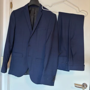 Mörkblå kostym med kavaj och byxor - Säljer en stilren mörkblå kostym med matchande kavaj och byxor. Kavajen har smal passform, tre knappar framtill och klassiska fickor. Perfekt för formella tillfällen eller bal. Vid frågor är det bara att höra av sig! Byxor i storlek 30, kavaj i storlek S 