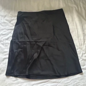 Svart satinkjol - Enkel svart kjol från BikBok i slät och glansig satin. Kjolen har rak passform och är kort i modellen, perfekt att styla med en cool topp eller en enklare T-shirt. Klassisk och stilren design utan detaljer. Passar till sommaren såväl som vintern! Använd en gång.