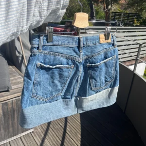 Jeanskjol - Jättefin jeanskjol med en rak volang, längd bak: 35cm, längd fram: 28cm, midjemått i knapphöjd: 37cm😊 hör gärna av er vid frågor🫶