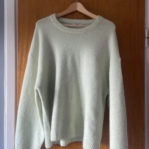 Ljusgrön stickad tröja från Gina Tricot - Mysig ljusgrön stickad tröja från Gina Tricot i storlek XL. Tröjan har rund halsringning, långa ärmar och ribbade muddar vid ärmslut och nederkant. Perfekt för kyligare dagar och enkel att matcha med olika outfits. Den har tyvärr en liten fläck på ärmen.