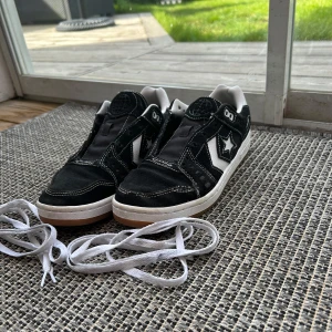 Svarta Converse CONS AS-1 Pro - Säljer ett par svarta Converse CONS AS-1 Pro med vita detaljer och stjärnlogga på sidan. Skorna har vit sula och skosnören ingår. Klassisk låg modell med rund tå och platt sula, perfekt för en streetwear-look. Dom har trådar som gått upp se bilder vänstra skon är värst men det är inget jag brytt mig om. Pris går att sänka vid snabb affär 