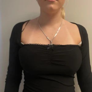 Svart långärmad topp med rosett - Säljer en svart långärmad topp med söt liten rosett framtill och rynkade detaljer vid bysten. Toppen har en feminin och figurnära passform med spetskant längs urringningen. Perfekt att styla till olika outfits!