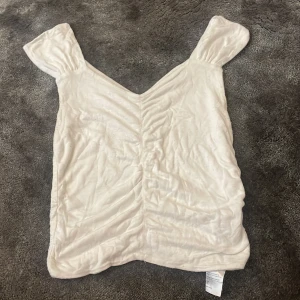 Vit omlott-liknande linnetopp - Säljer en söt vit linnetopp med breda axelband och v-ringad omlottliknande framsida. Toppen har en lätt rynkad effekt längs mitten.