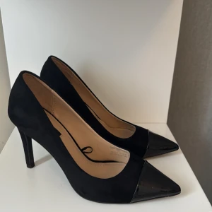 Svarta klackar från Zara Trafaluc - Snygga svarta klackar med spetsig tå från Zara Trafaluc. Skorna har hög klack och en kombination av mockaliknande material och glansig tå i syntet. Perfekta för dig som vill ha en stilren och elegant look.