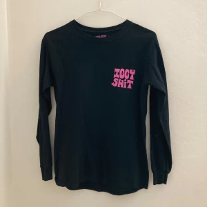Svart långärmad tröja med rosa tryck från Iggy Shit - Cool svart långärmad tröja med rosa texttryck både fram och bak. Trycket på bröstet och ryggen har en lekfull, grafisk stil. Perfekt för dig som gillar statement-plagg och streetwear.