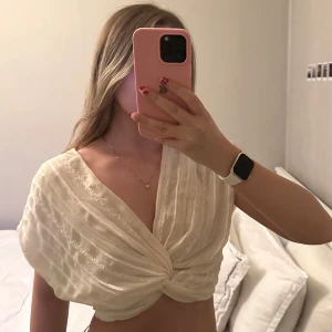 Krämvit omlottopp från Zara - Säljer en krämvit omlottopp från Zara med glittriga ränder och twistad knut framtill. Toppen är croppad och har v-ringning samt korta ärmar🤍Använd 1-3 gånger, inga defekter (som ny)!