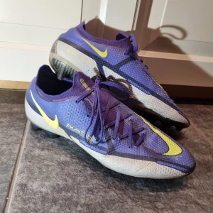 Nike Phantom GT2 Elite fotbollsskor - Säljer ett par Nike Phantom GT2 Elite fotbollsskor. Använda skor så de är rätt slitna (se defekter på övriga bilder) De vita som syns på framsidan är en signering från Ruben Dias då jag vann skorna på en insta-tävling men spelade med skorna Pris kan diskuteras vid snabb affär Nypris: 2799 kr