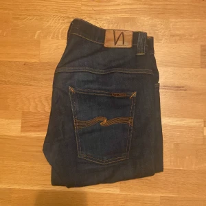 Mörkblå jeans från Nudie Jeans - Säljer ett par mörkblå jeans från Nudie Jeans med klassiska orange sömmar och Nudie-logga på bakfickan. Skick 8/10. Jag är 182 och väger 70 kg och det sitter bra! Hör av er vid frågor! ❤️👍🏻🙌