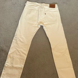 Vita Levi's 501 jeans - Säljer ett par klassiska vita Levi's 501 jeans med raka ben och knappgylf. Byxorna har fem fickor och den ikoniska läderpatchen bak i midjan. Perfekta för dig som vill ha en tidlös och clean look. (Pris kan diskuteras vid snabb affär)