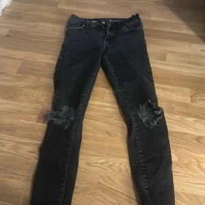 Svarta skinny jeans med slitningar - Svarta skinny jeans med slitna detaljer över knäna. Klassisk femficksmodell med knapp och dragkedja framtill. Snygg passform som sitter tight hela vägen ner.