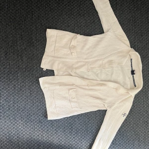 Vit grisch kofta Pelle P - Säljer en klassisk vit kofta från Pelle P med ribbad struktur och två fickor framtill. Koftan har långa ärmar och stängs med knappar. Perfekt för lager-på-lager och enkel att matcha. Riktigt Grisch!