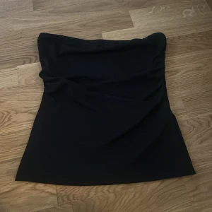 Svart tubtopp från 157 - Säljer en svart tubtopp från 157. Enkel och stilren design utan axelband, perfekt att matcha med olika outfits. Tillverkad i mjukt material som sitter bekvämt mot kroppen.