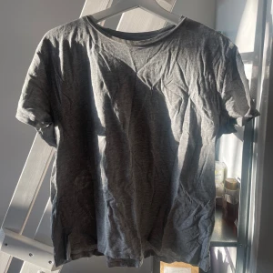 Grå t-shirt från 157 - En basic grå t-shirt från 157 i storlek L. Tillverkad i mjuk bomullsblandning med 90% bomull och 10% viskos. Klassisk passform med rund hals och korta ärmar. Perfekt till vardags eller som lager under skjorta.