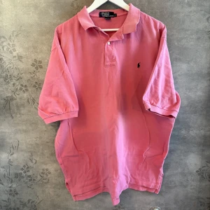 Ralph Lauren Piké - Säg hej till sommaren med stil!  Denna rosa pikétröja från Ralph Lauren är en riktig vibe - perfekt färg, klassisk passform och ett extra broderi på ärmen för det lilla extra.  Ralph Lauren, Polo Ralph Lauren, Pikétröja herr, Preppy stil, Klassisk piké, Designer piké, Streetwear, Herrmode, Loggopiké, Sommarstil, Snygg piké, Trendigt plagg.  #ralphlauren #rosapiké #sommarstil #preppy #herrmode #statementpiece  Storlek: L (hade passat xl/xxl) Skick: Bra - mjuk och bekväm Pris: 240kr