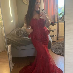 Röd långklänning med spets från Dressroom - Säljer en elegant röd långklänning från Dressroom med v-ringning och spetsdetaljer. Klänningen har volang i midjan och är ärmlös, perfekt för bal eller festliga tillfällen. Köptes för 5000 säljer för 3500 pga bara använd 1 gång