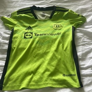 Manchester United fotbollströja Ronaldo 7 - Säljer en neongul Manchester United fotbollströja med svarta detaljer, Adidas-logga och TeamViewer sponsortryck. Nummer 7 och Ronaldo på ryggen. Kortärmad modell i lätt material, perfekt för fotbollsträning eller match.