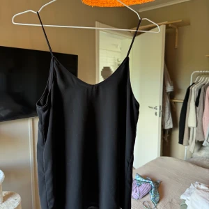 Svart linne med smala axelband från Vero Moda - Linne från Vero Moda med smala axelband. Tunn och lätt i materialet.