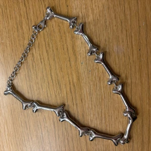Silverfärgat halsband med benformade länkar - Unikt halsband i silverfärg med länkar formade som små ben. Kedjan har justerbar längd och stängs med karbinhake. Perfekt statement-piece för dig som gillar annorlunda smycken.