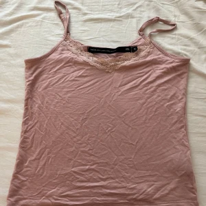 Rosa linnetopp med spets från 157 - Supersöt ljusrosa linnetopp från 157 med tunna axelband och spetsdetalj vid ringningen. Toppen är armlös och har en mjuk, följsam känsla i bomullsmix. Perfekt att styla med jeans eller kjol för en chill look.