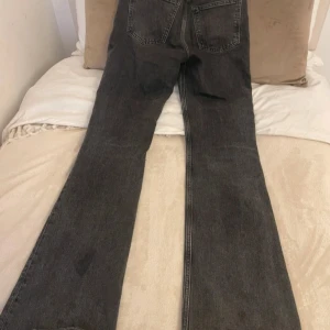 Svarta bootcut jeans med slitning - Säljer ett par svarta bootcut jeans med snygg slitning på ena knät. Jeansen har klassisk femficksdesign, hög midja och raka ben som går ut i en bootcut. Perfekta för dig som gillar en avslappnad och trendig look.