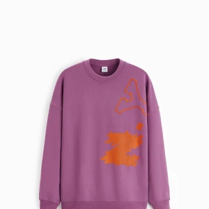Lila sweatshirt från Zara med orange tryck - Säljer en oversized lila sweatshirt från Zara med coolt orange grafiskt tryck på framsidan. Tröjan har rund hals, långa ärmar och är gjord i mjuk bomull. Perfekt för dig som gillar färg och streetstyle.
