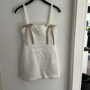 Vit satin klänning med rosetter Zara - Kort vit klänning i satin från zara. Helt oanvänd med prislapp kvar.