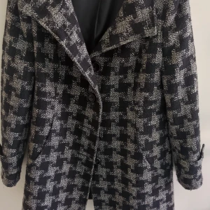 Rutig svart och vit kappa med knappar - Snygg kappa i svart och vitt med rutigt mönster och stora knappar framtill. Jackan har bred krage, långa ärmar och är tillverkad i ett grovt tyg som känns både stilrent och trendigt. Perfekt för dig som vill sticka ut med ett klassiskt men edgy plagg.