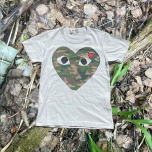 Comme des Garçons Camo T-shirt  - Säljer nu denna eftertraktade T-shirten från Play Comme des Garçons. Den har en stor logga på bröstet med ett camouflage mönster och sedan en mindre broderad logga som är röd. | Den är riktigt bra skick då den endast är använd ett fåtal gånger. | Den är i storlek S men jag skulle säga att den även passar som en XS. | Det är bara att höra av sig om man har några frågor eller om man vill ha flera bilder.