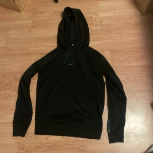 Svart Nike hoodie XS med logga - Svart hoodie från Nike i storlek XS. Klassisk design med huva och Nike-logga på bröstet samt tryckt Nike-band längs båda armarna. Mjuk och skön polyester, perfekt för chill eller träning. Långärmad och med ribbade muddar för extra komfort.